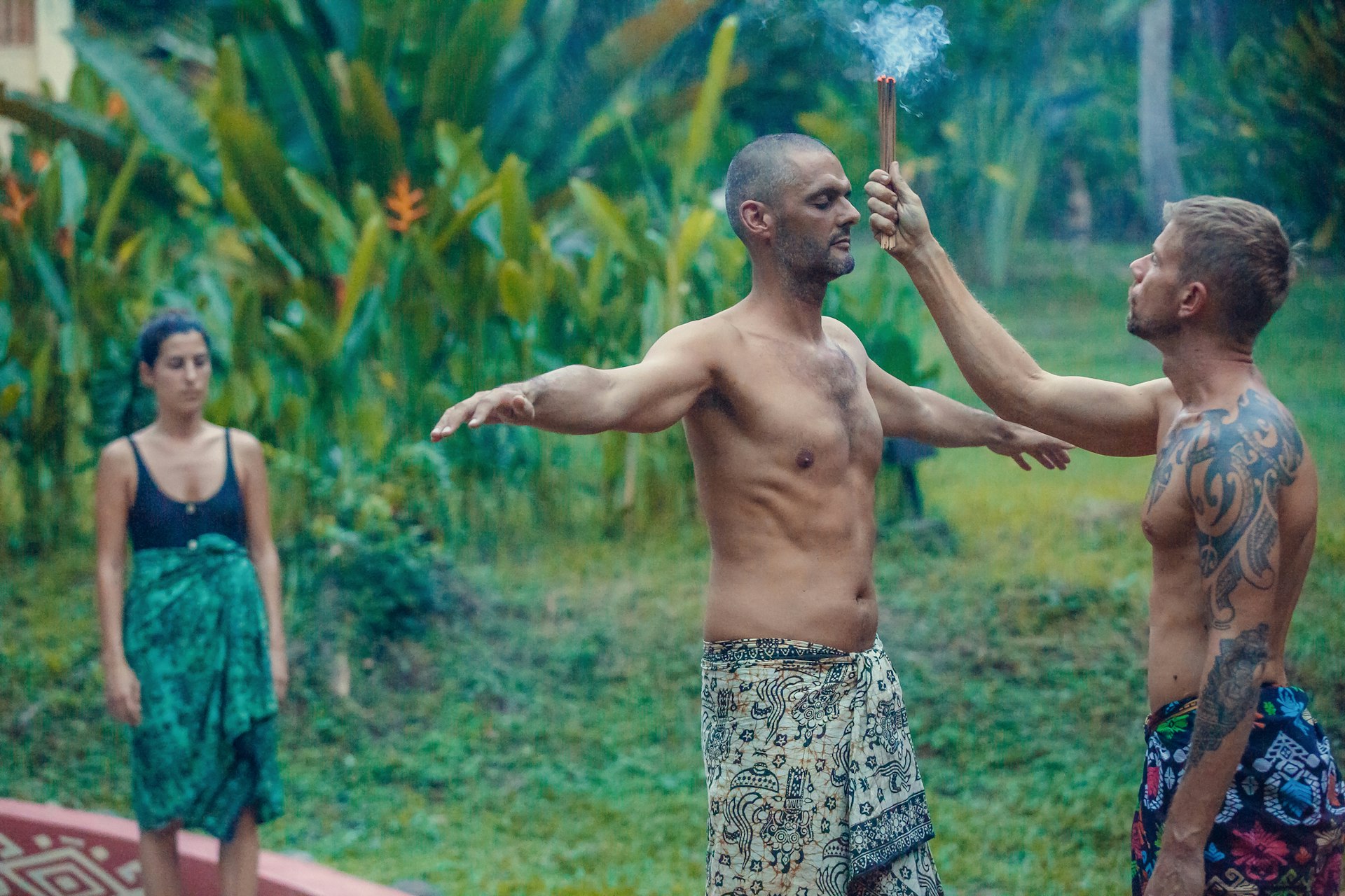A man stands before a Shaman in a jungle setting while smoke is wafted over his head